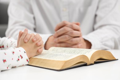 Photo of Girl and her godparent praying over Bible together at table indoors, closeup