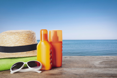 Image of Set of sun protection products and stylish accessories on wooden table near sea. Space for text