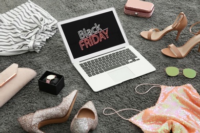 Photo of Laptop with Black Friday announcement surrounded by clothes and accessories on grey carpet