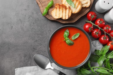 Flat lay composition with delicious tomato cream soup in bowl on grey textured table. Space for text