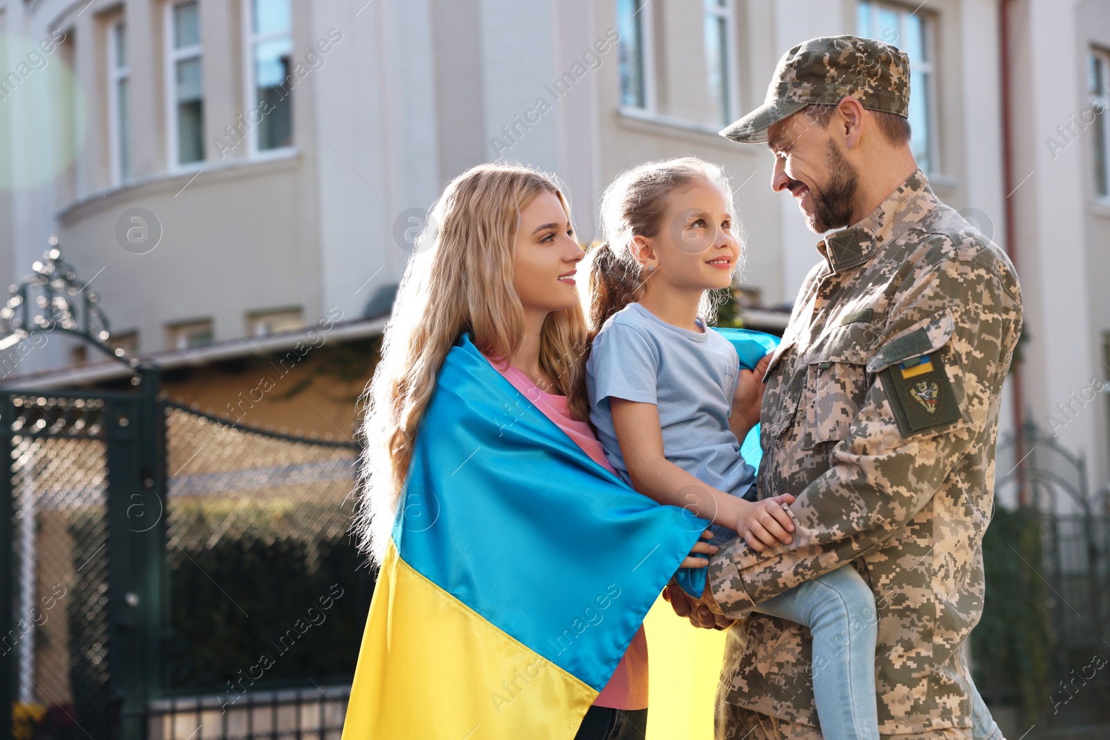 Photo of Soldier in military uniform reunited with his family and Ukrainian flag outdoors