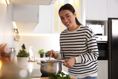 Photo of Smiling woman with wooden spoon cooking soup in kitchen