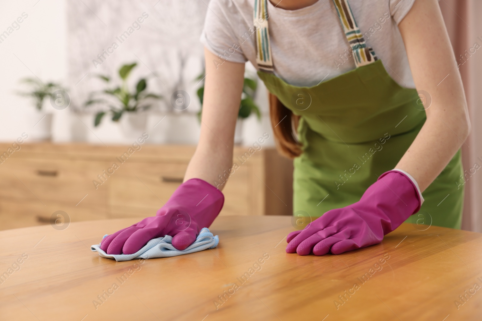 Photo of Woman with microfiber cloth cleaning wooden table in room, closeup