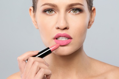 Young woman applying beautiful lipstick on gray background