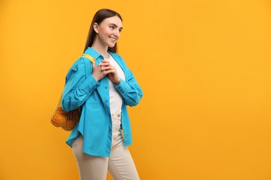 Woman with string bag of fresh oranges on orange background, space for text