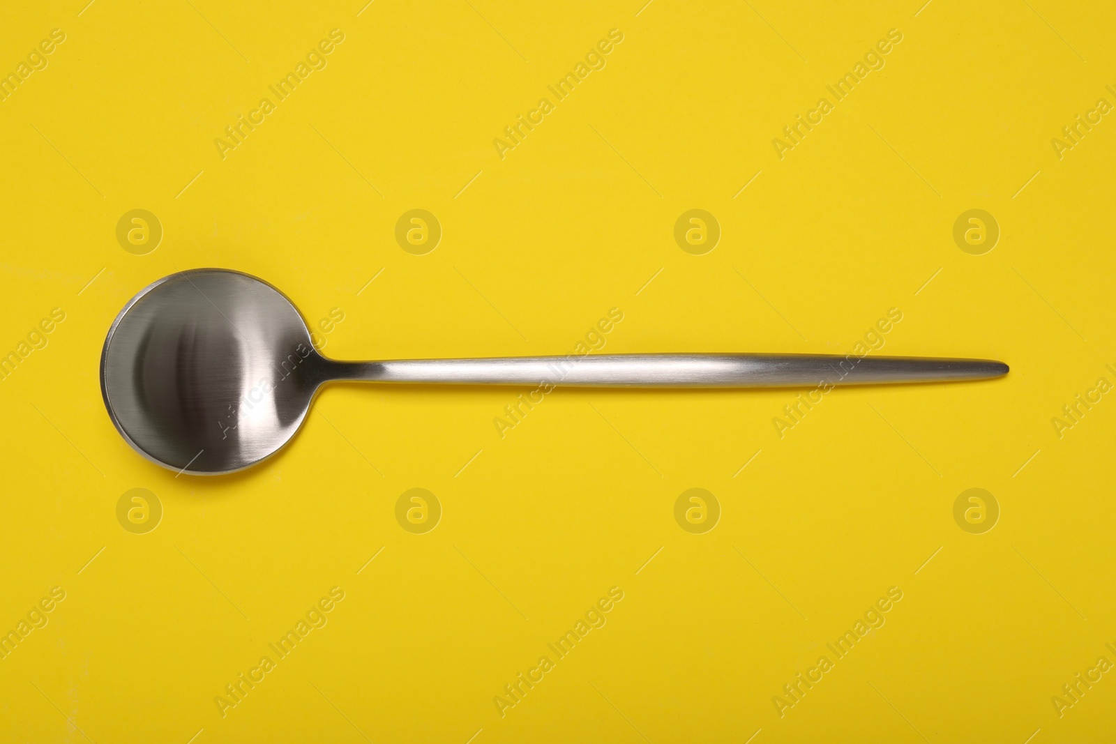 Photo of One shiny silver spoon on yellow background, top view