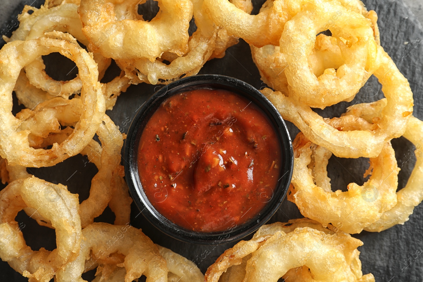 Photo of Delicious golden crispy onion rings and sauce on gray background, top view