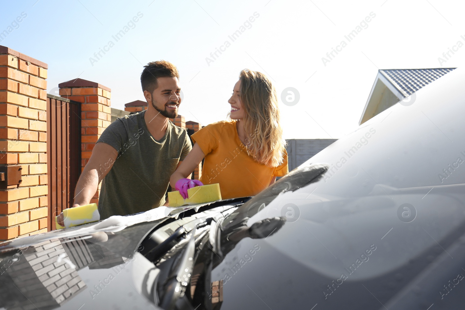 Photo of Happy young couple washing car at backyard on sunny day