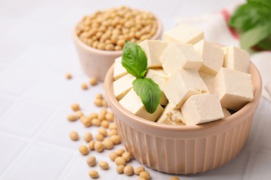 Photo of Delicious tofu cheese, basil and soybeans on white tiled table, closeup. Space for text
