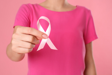 Woman holding pink ribbon on color background, closeup. Breast cancer awareness