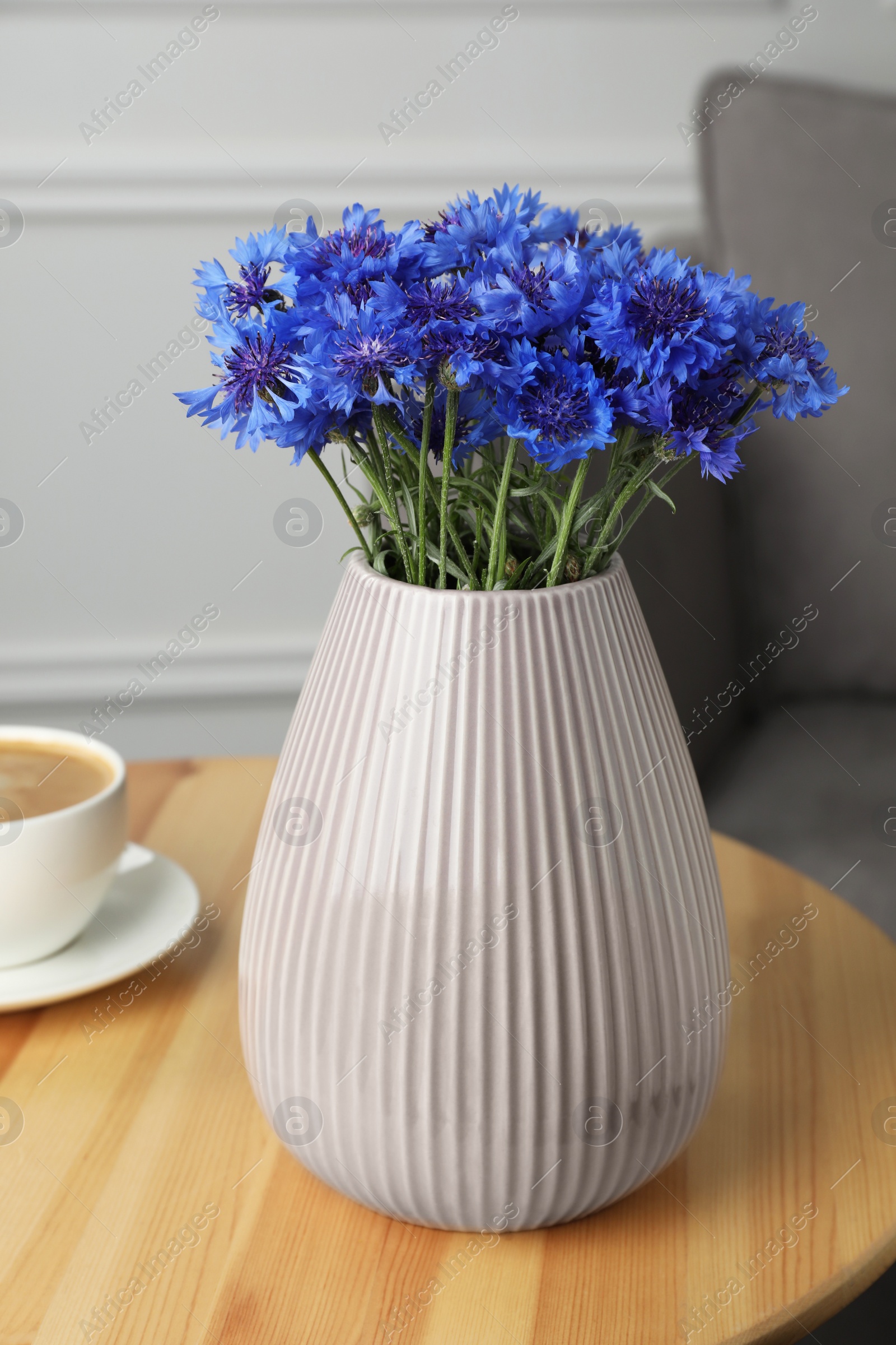 Photo of Bouquet of beautiful cornflowers in vase on wooden table at home