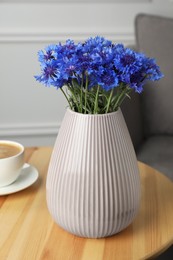 Bouquet of beautiful cornflowers in vase on wooden table at home