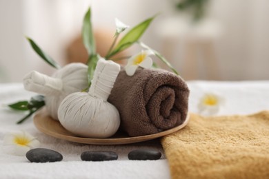 Spa stones, flowers and herbal bags on towel indoors, closeup