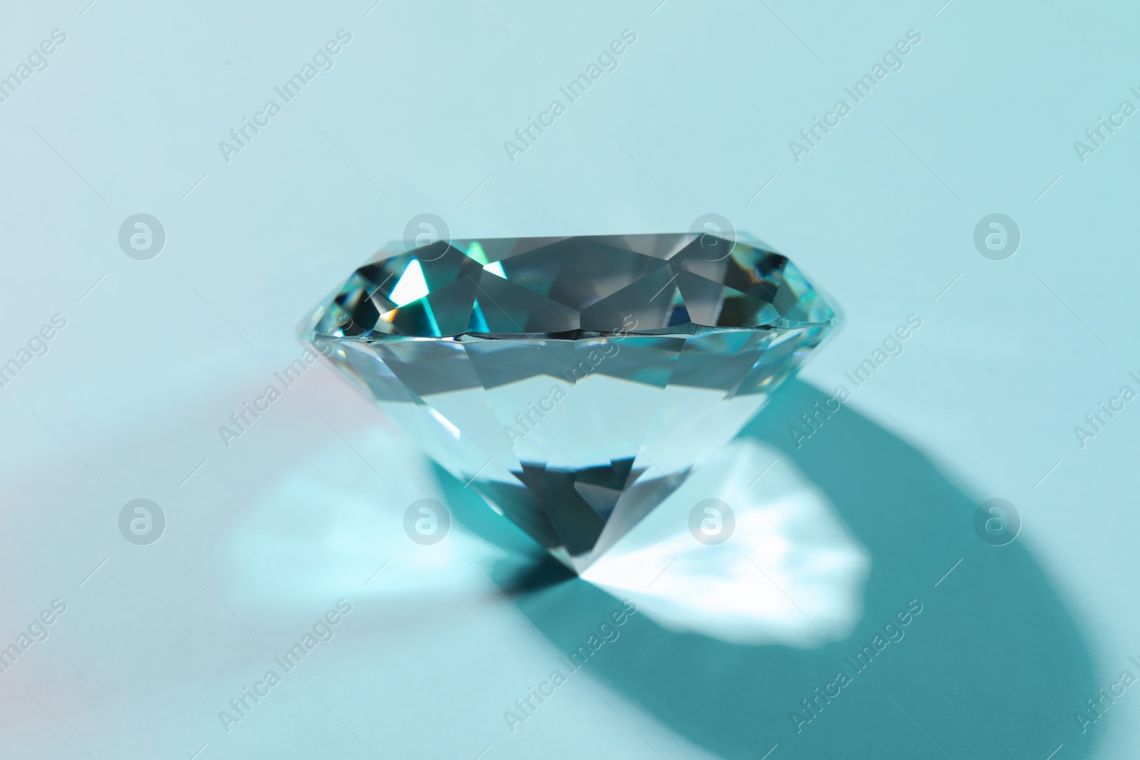 Photo of Beautiful dazzling diamond on turquoise background, closeup