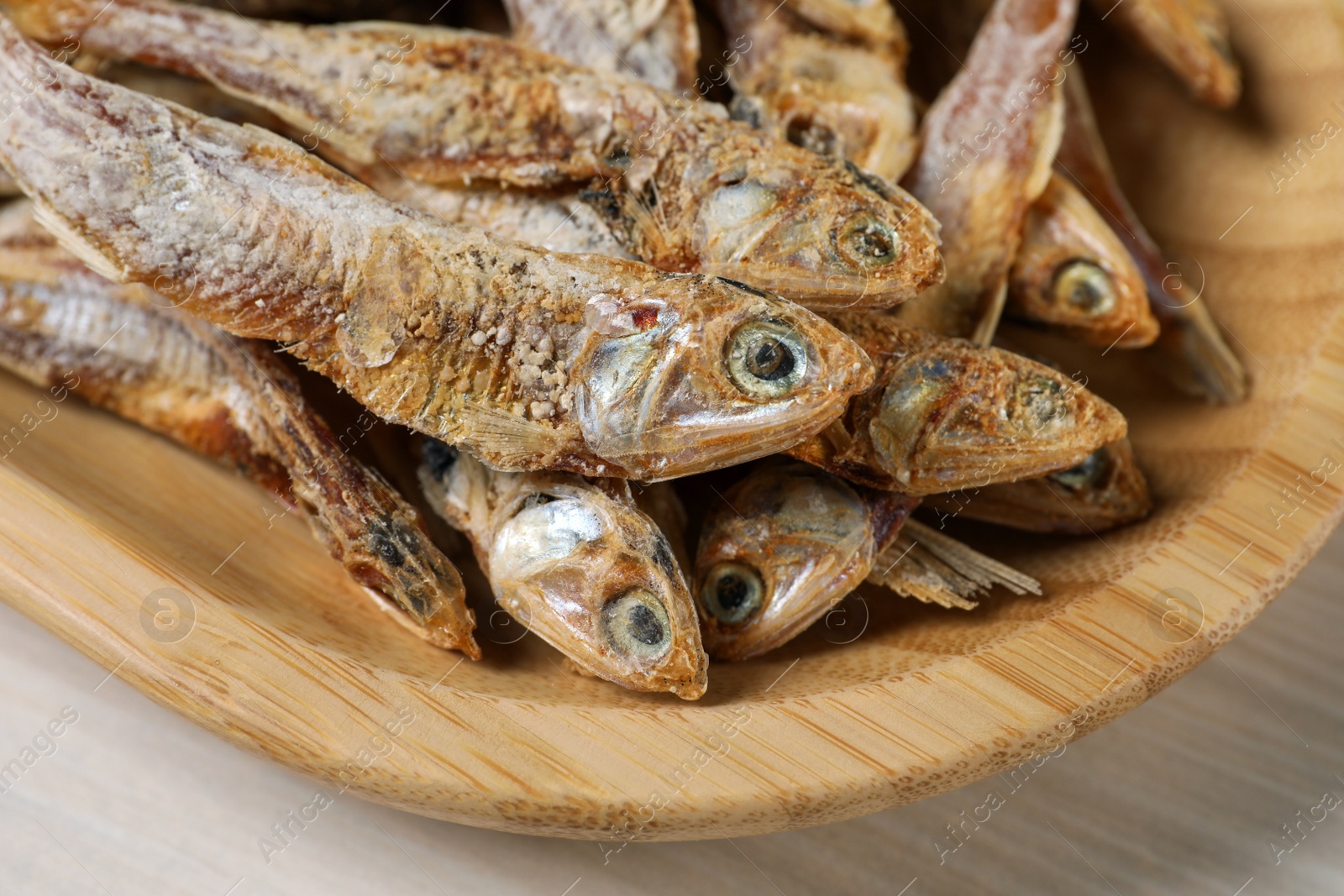 Photo of Wooden plate of tasty dried anchovies on table, closeup