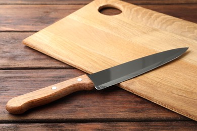 Photo of One sharp knife and board on wooden table, closeup