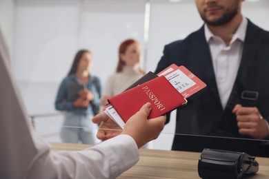 Photo of Agent giving passports with tickets to client at check-in desk in airport, closeup