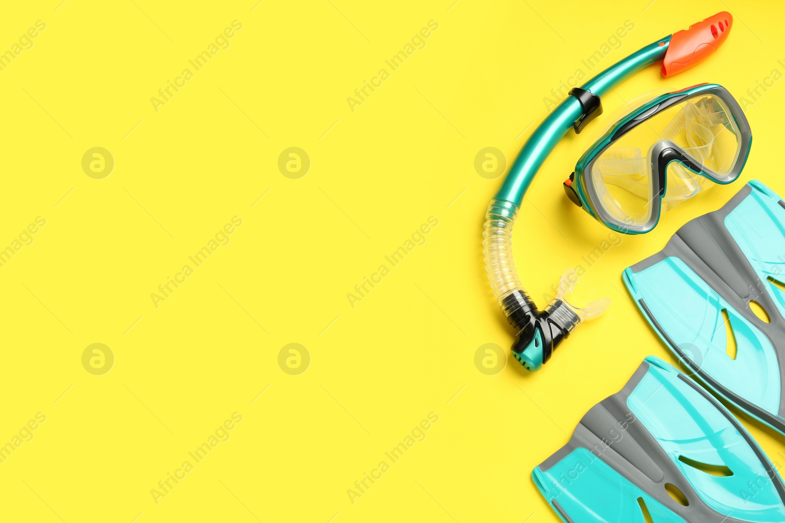 Photo of Pair of turquoise flippers and mask on yellow background, flat lay. Space for text