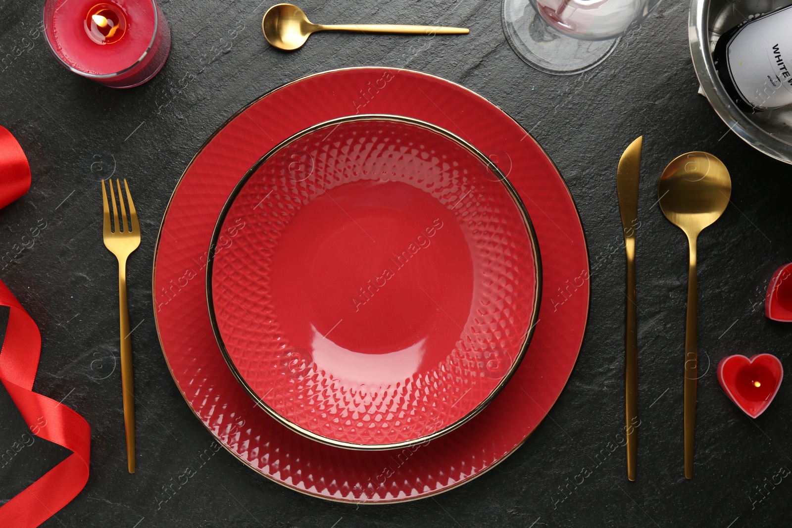 Photo of Romantic place setting with candles and red ribbon on dark gray textured table, flat lay