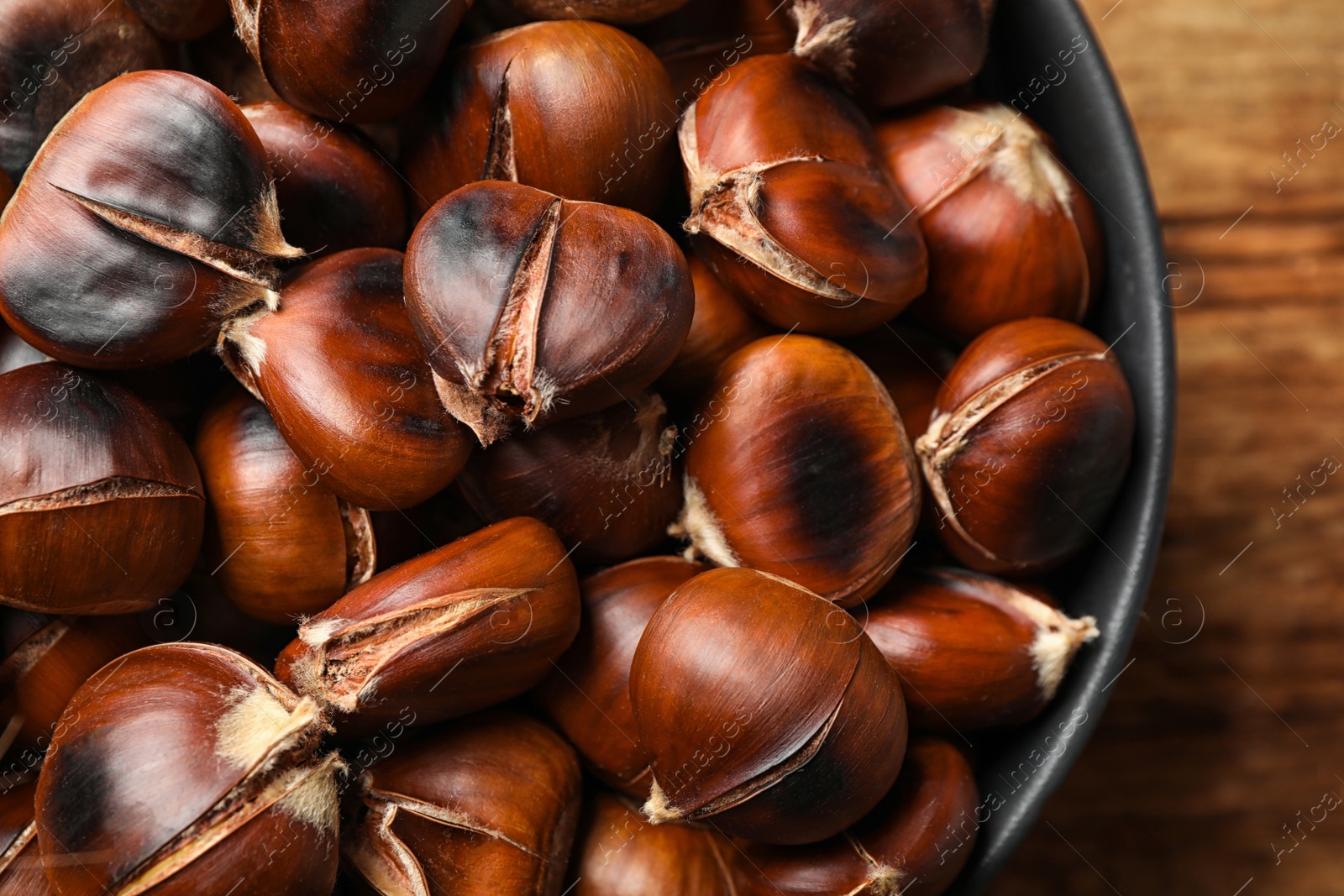 Photo of Delicious roasted edible chestnuts in bowl on table, top view