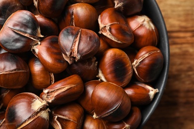 Photo of Delicious roasted edible chestnuts in bowl on table, top view