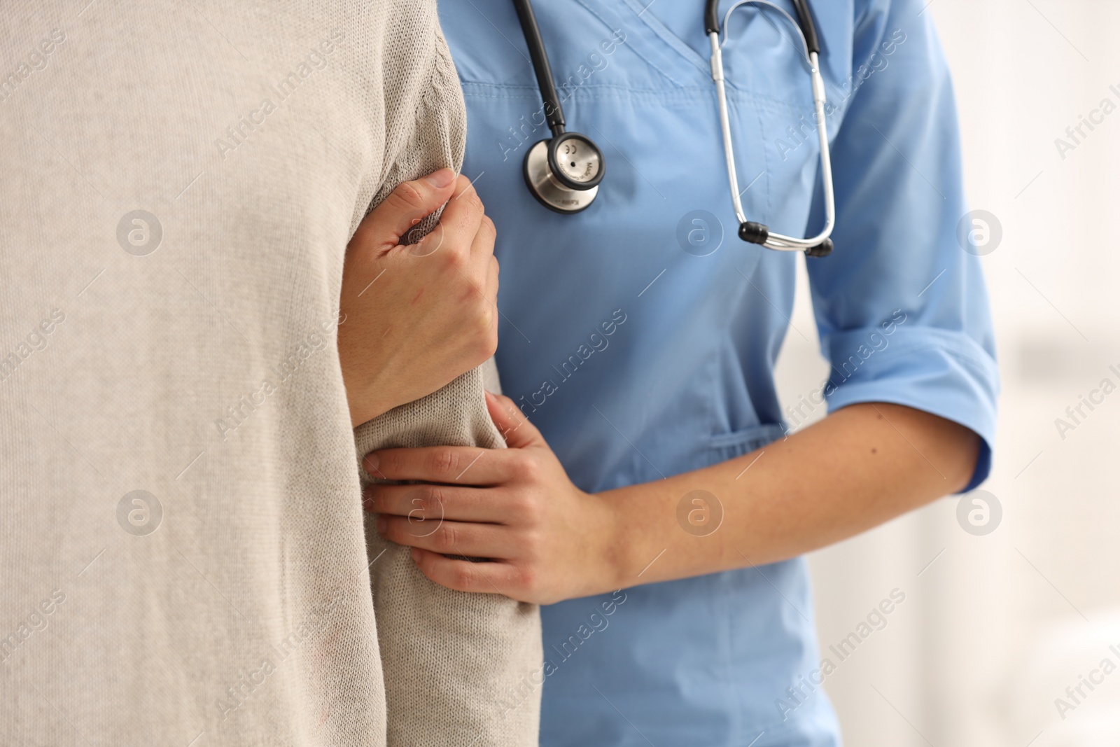 Photo of Nurse supporting elderly patient indoors, closeup view