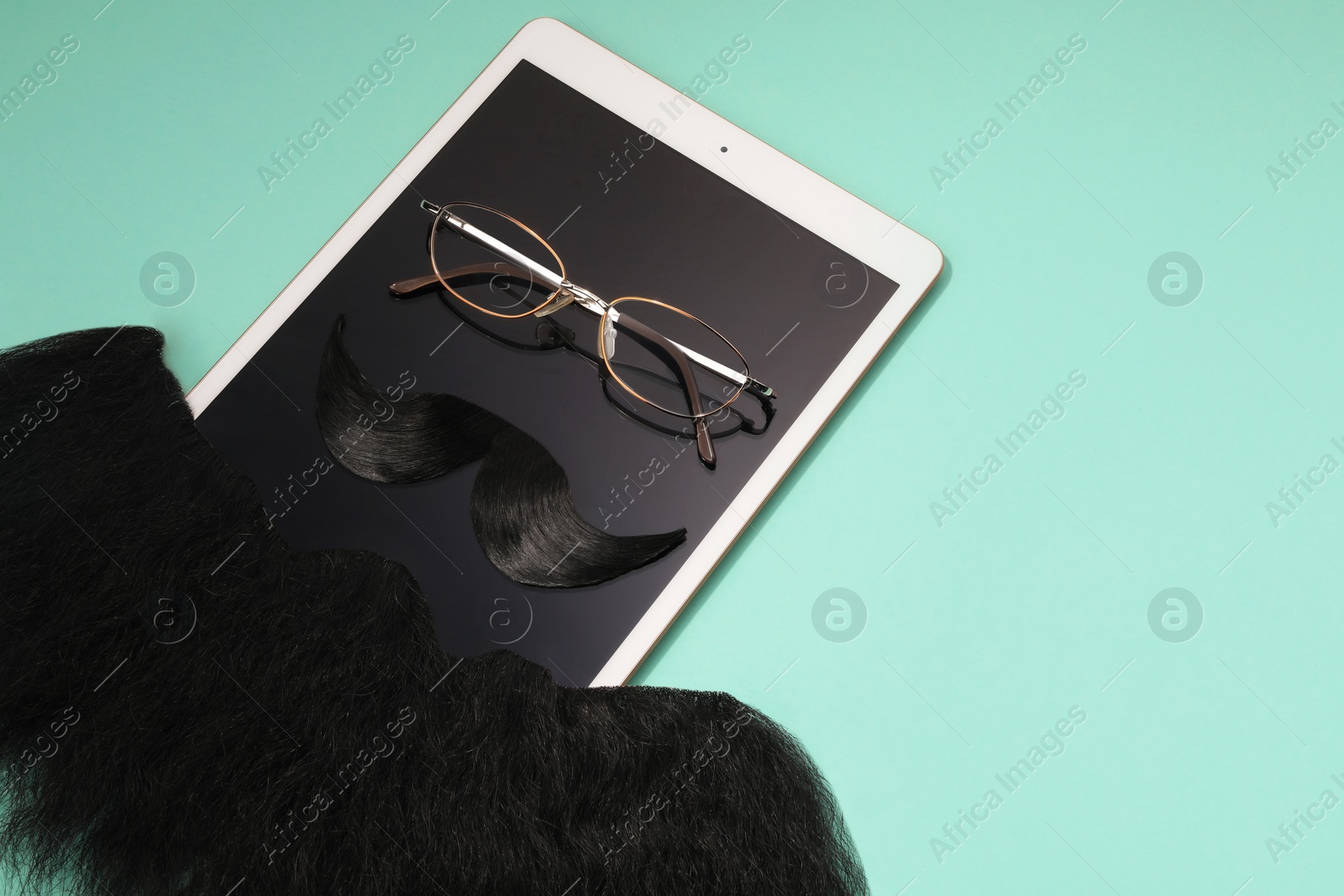 Photo of Artificial moustache, beard, tablet and glasses on turquoise background, above view. Space for text