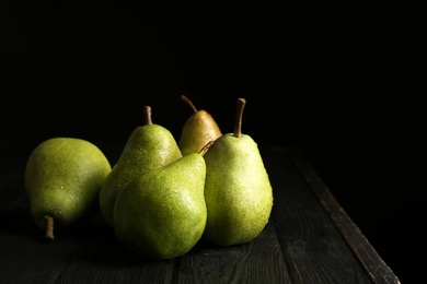 Photo of Ripe pears on wooden table against dark background. Space for text