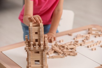 Photo of Little girl playing with wooden tower at table indoors, closeup. Child's toy