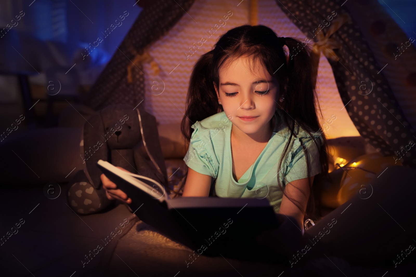 Photo of Little girl reading fairy tale in play tent at home