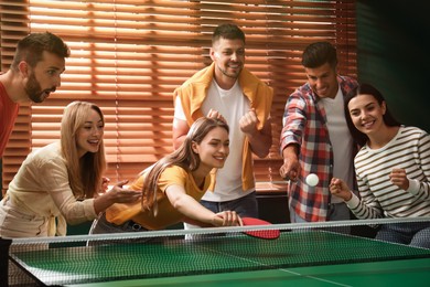 Photo of Happy friends playing ping pong together indoors