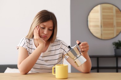 Photo of Sleepy young woman pouring coffee into cup at wooden table indoors
