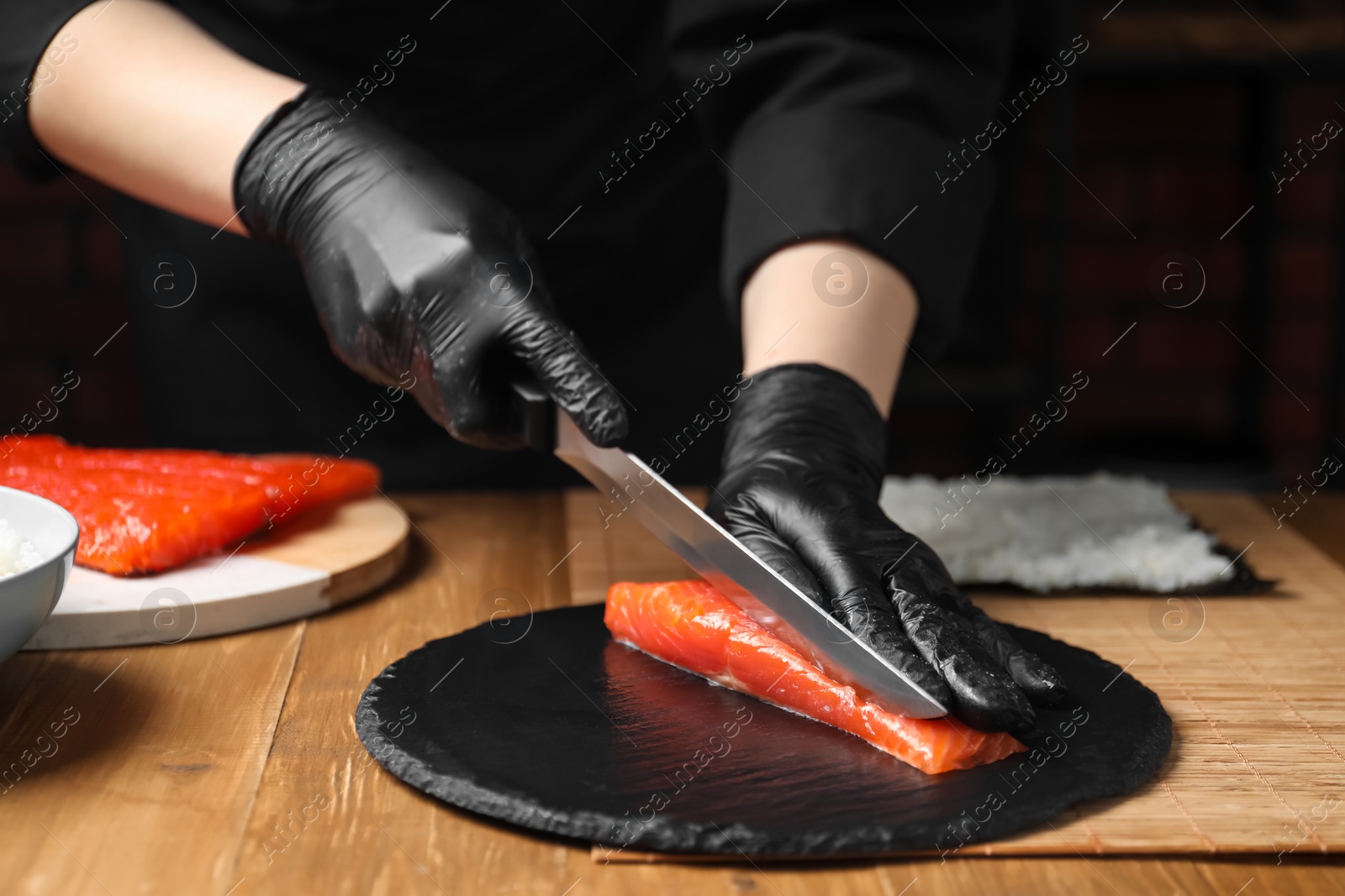 Photo of Chef in gloves cutting salmon for sushi at wooden table, closeup