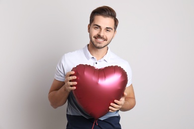 Photo of Portrait of young man with heart shaped balloon on light background