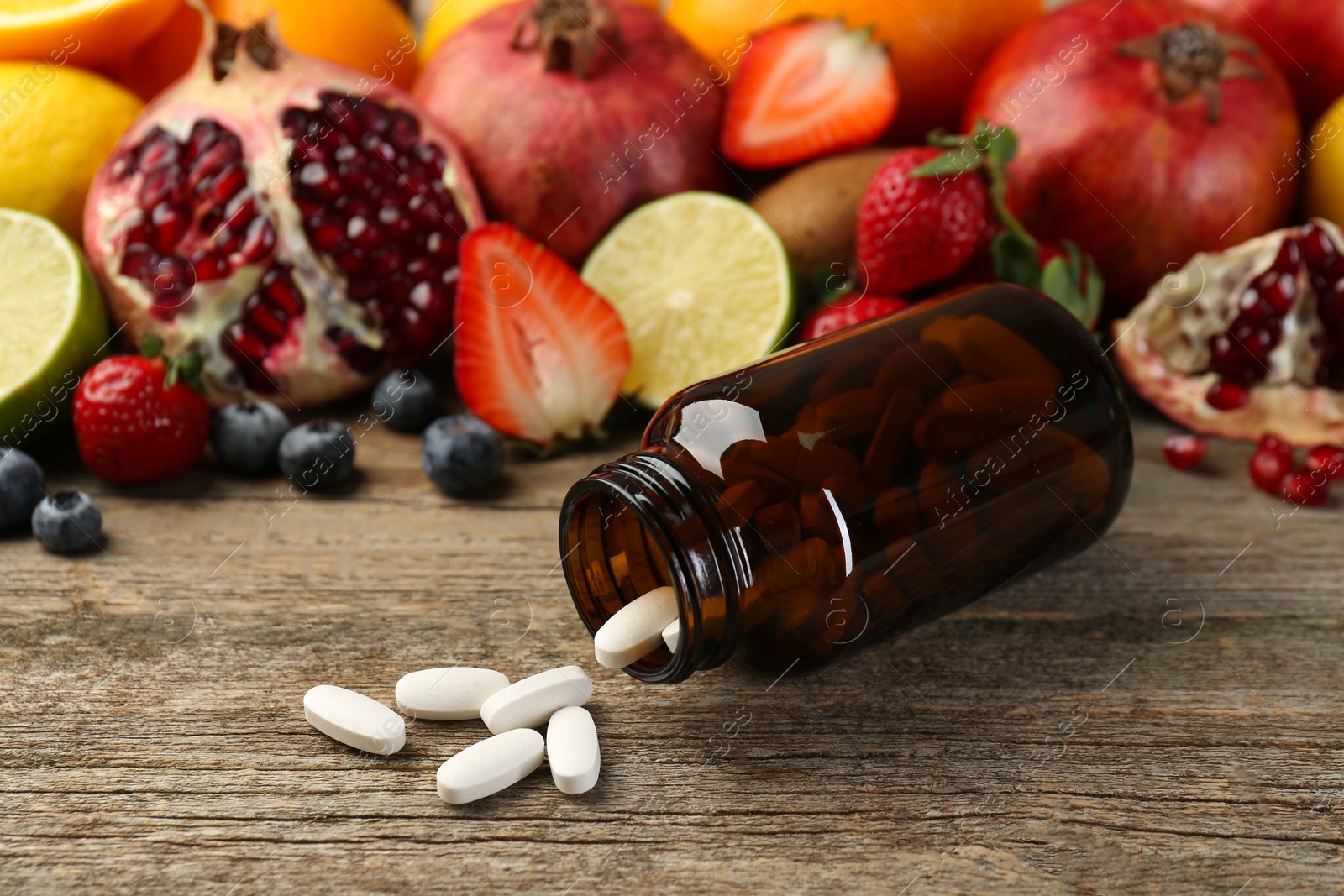 Photo of Vitamin pills, bottle and fresh fruits on wooden table