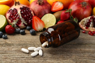 Photo of Vitamin pills, bottle and fresh fruits on wooden table