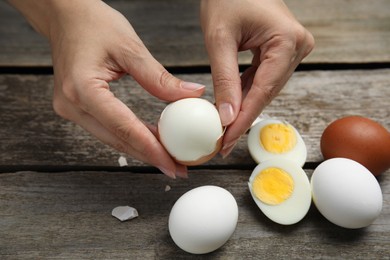 Woman peeling boiled egg at wooden table, closeup