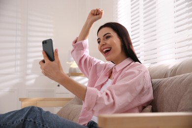 Photo of Emotional woman participating in online auction using smartphone at home
