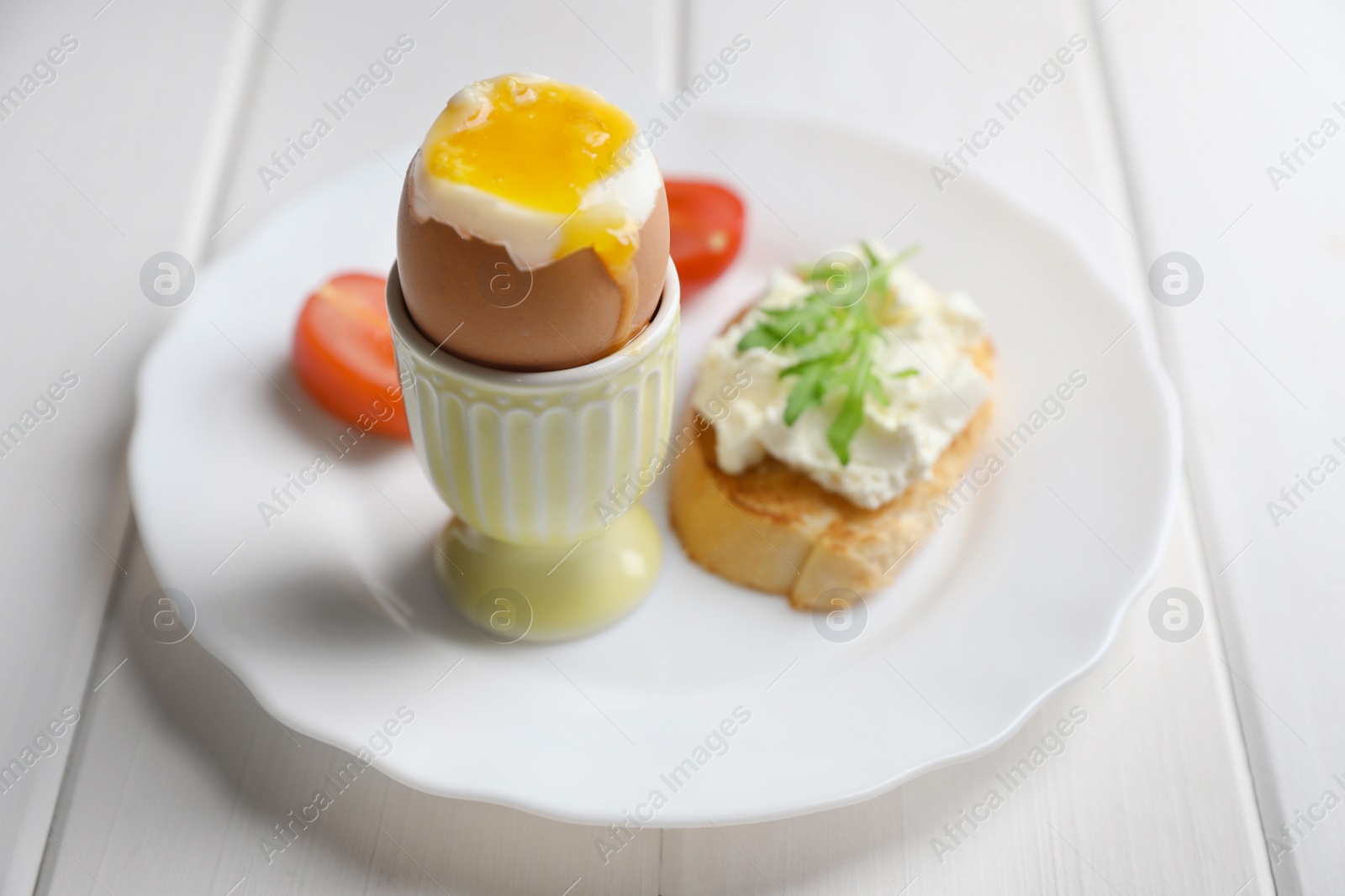 Photo of Fresh soft boiled egg in cup and sandwich on white wooden table