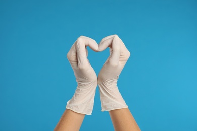 Doctor in medical gloves showing heart with hands on light blue background, closeup