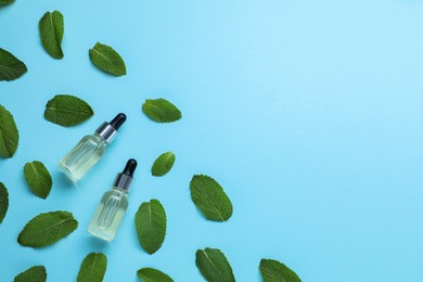 Photo of Bottles of essential oil and mint on light blue background, flat lay. Space for text
