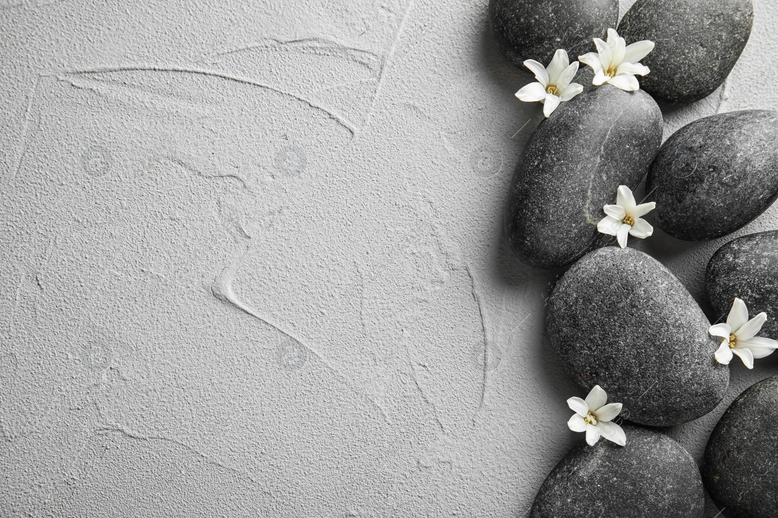 Photo of Zen stones and exotic flowers on grey background, top view with space for text