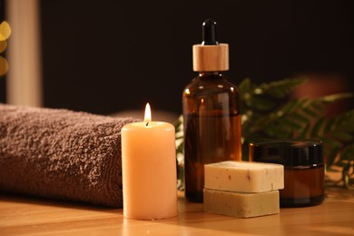 Photo of Spa composition. Cosmetic products, burning candle and towel on wooden table