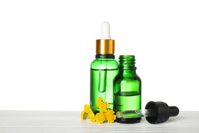 Bottles of essential oil and flowers on wooden table, white background