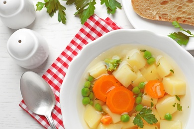 Photo of Bowl of fresh homemade vegetable soup served on white wooden table, flat lay