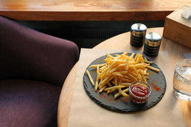 Photo of Tasty French fries with red sauce served on table in cafe