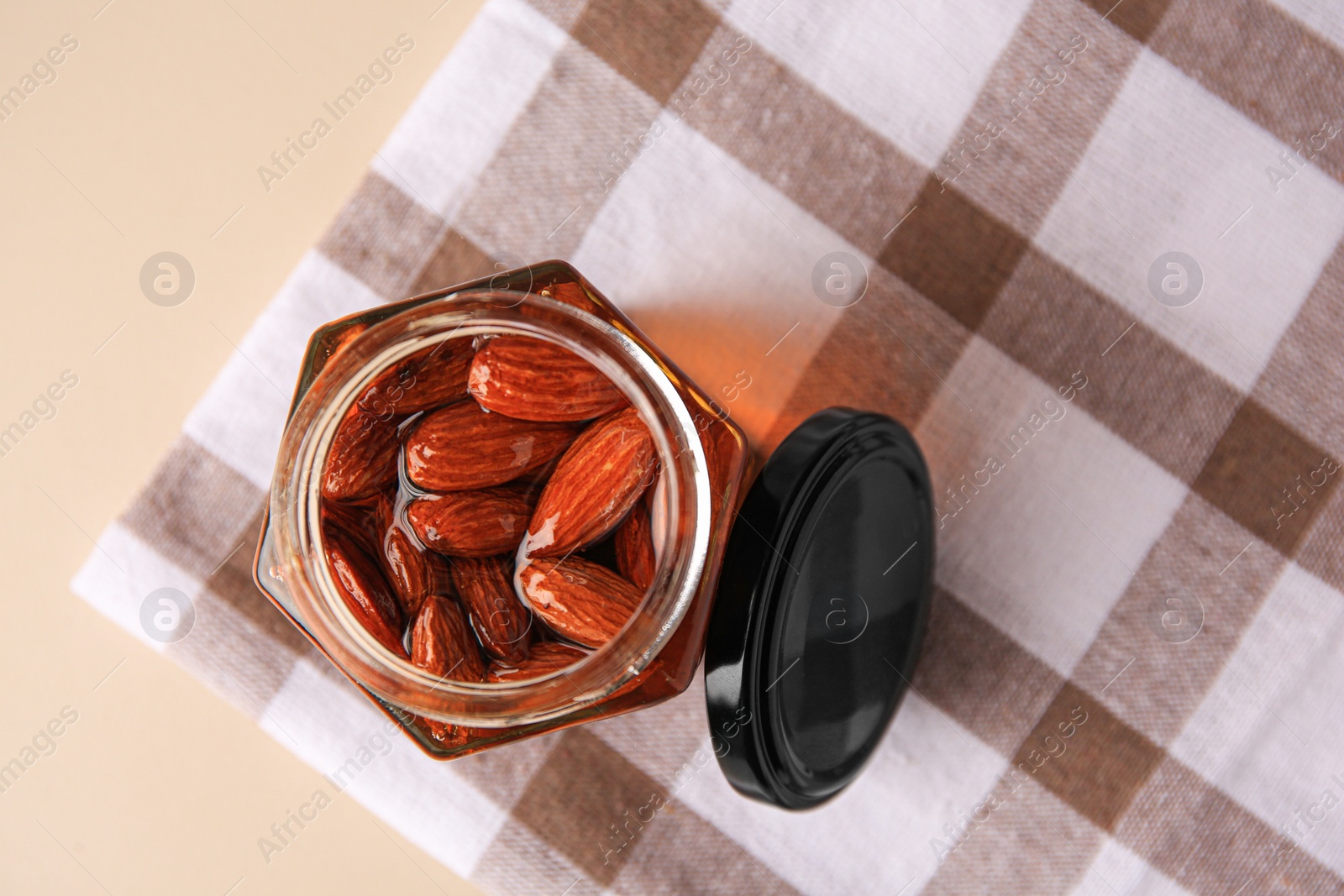 Photo of Jar with almonds and honey on beige table, top view. Space for text