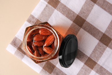 Photo of Jar with almonds and honey on beige table, top view. Space for text