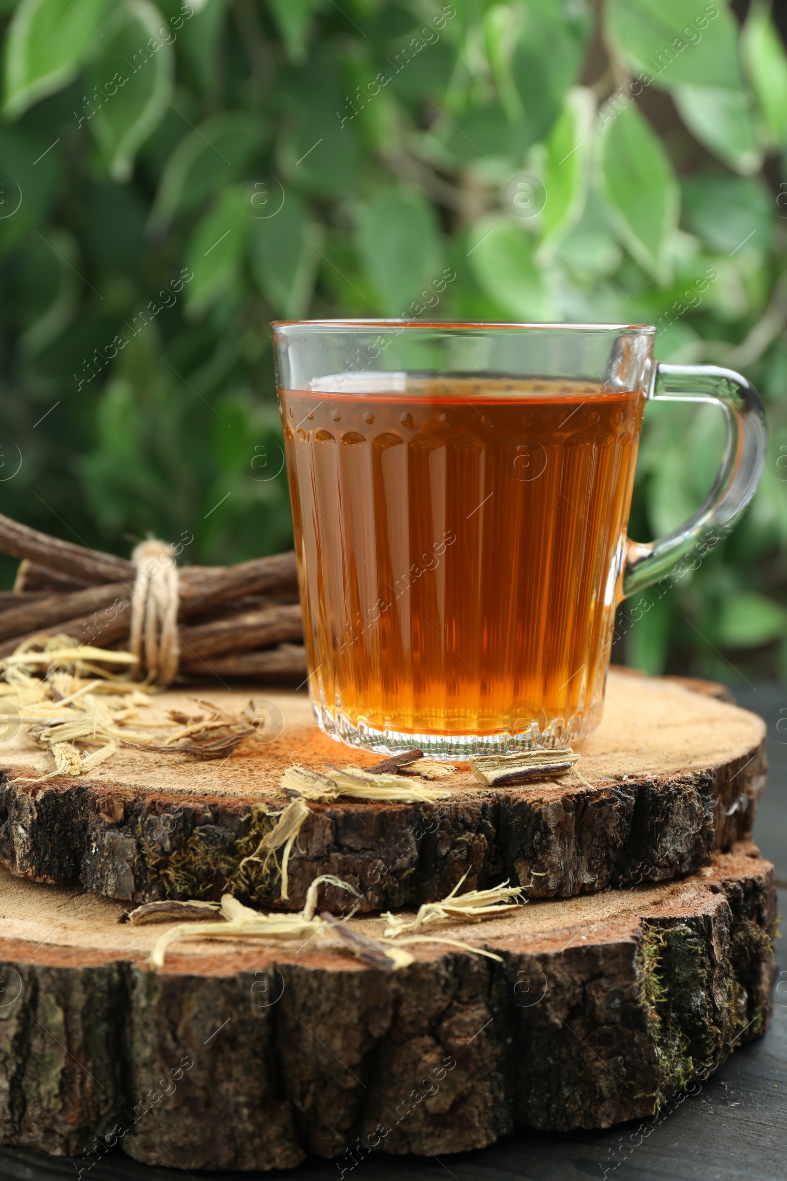 Photo of Aromatic licorice tea in cup and dried sticks of licorice root on black table, closeup