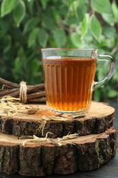 Aromatic licorice tea in cup and dried sticks of licorice root on black table, closeup